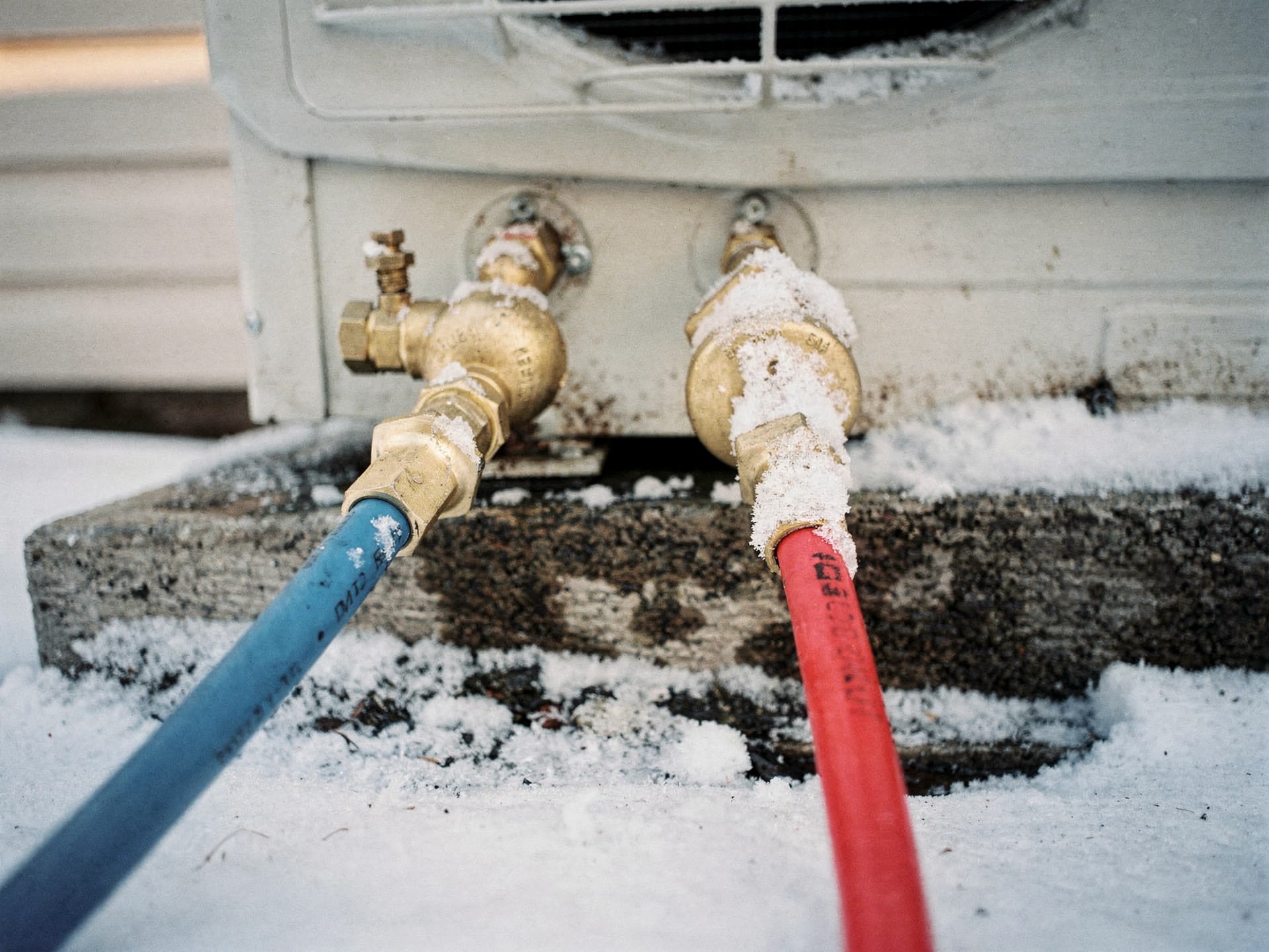 Blue and red gauge hoses coupled to the service valves on a snow covered outdoor unit